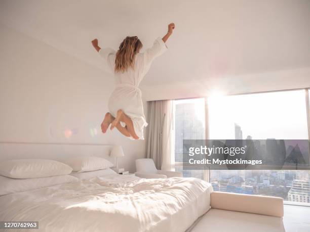 vrouw die op bed in hotelruimte springt - jumping on bed stockfoto's en -beelden