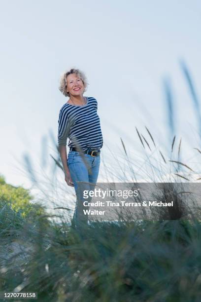 mature, attractive woman stands on a dune on the beach. - wadden sea stock pictures, royalty-free photos & images