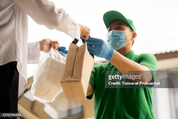 delivery service man in green uniform handing fresh food to recipient and young woman customer receiving order from courier at home. - man offering bread stock pictures, royalty-free photos & images