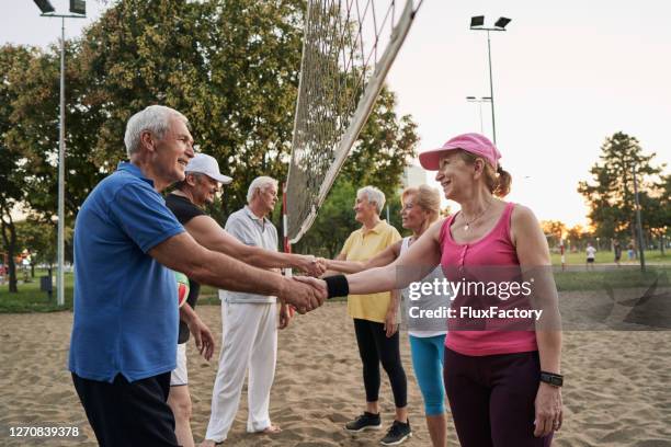 active senior sports teams greeting each other before a beach volleyball match - volleyball park stock pictures, royalty-free photos & images