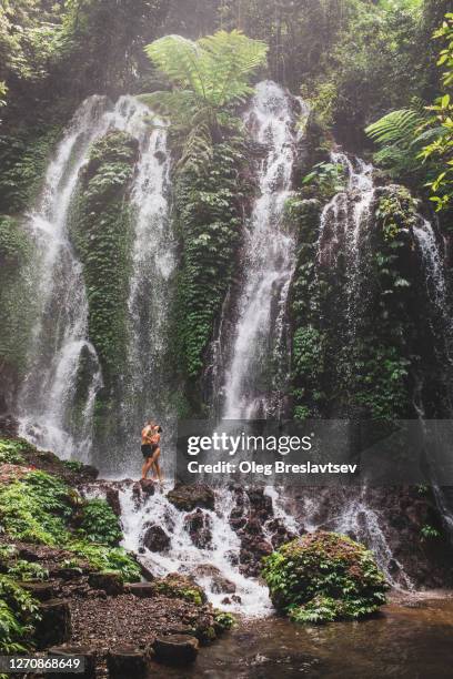 couple kissing against huge tropical waterfall in bali jungle - bali waterfall stock pictures, royalty-free photos & images