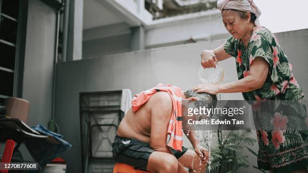 asian chinese senior woman washing cleaning her husband hair , hairwash at front yard of the house when there is no water supply