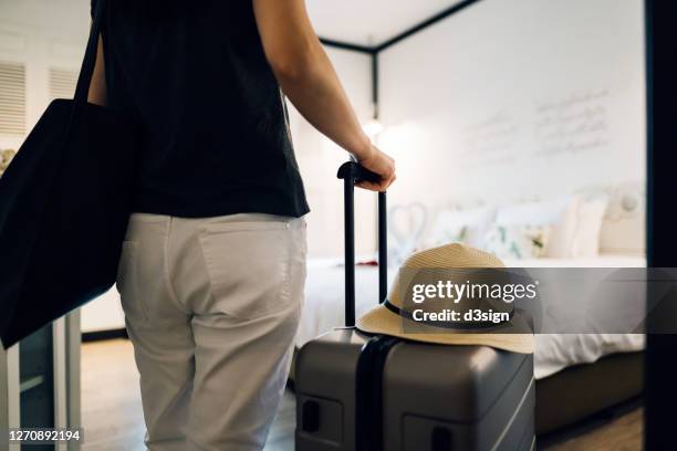 rear view of young asian female traveller entering the hotel room at the hotel. she is carrying a suitcase with a straw hat and is on summer vacation - city break stock pictures, royalty-free photos & images