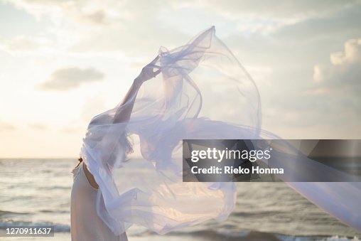 Woman holding white sheer fabric on the beach Woman holding white sheer fabric on the beach