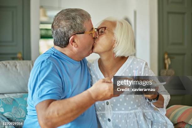 pareja mayor besándose y sosteniendo pastel de cumpleaños en casa - beso en la boca fotografías e imágenes de stock