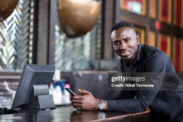 a freelancer sitting at a restaurant bar using his smartphone, smiling looking at the camera. - social media profile stock pictures, royalty-free photos & images