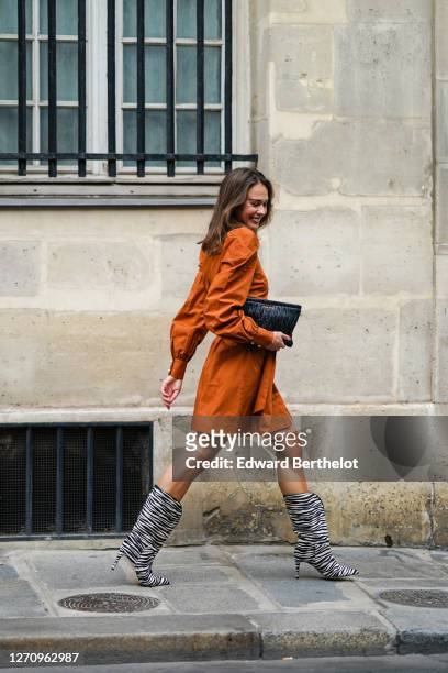 Therese Hellström wears an orange short dress with puff sleeves from Custommade, a black leather quilted bag from Miu Miu, black and white zebra...