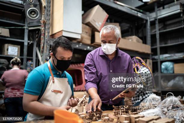 senior carpenter teaching young employee, both wearing face mask - covid persons with disabilities stock pictures, royalty-free photos & images