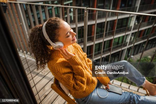 ung kvinna med hörlurar lyssnar musik på balkongen - dominican ethnicity bildbanksfoton och bilder