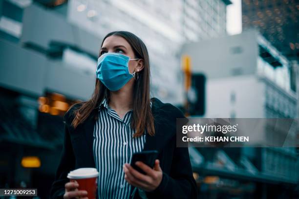 caucasian white businesswoman with protective face mask holding smartphone and coffee cup walking on the street in rush hour during covid-19 - auckland covid stock pictures, royalty-free photos & images