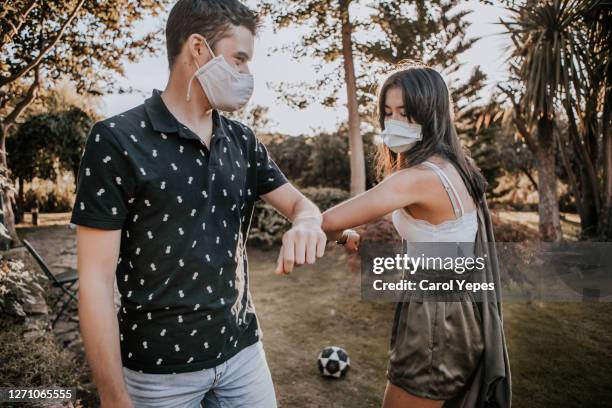 young couple wearing disposable face masks meeting in outdoors.. elbow bump - coronavirus dating stock pictures, royalty-free photos & images