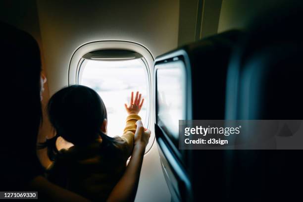 young asian mother and excited little daughter looking out through window in airplane while travelling on holiday - take care foto e immagini stock
