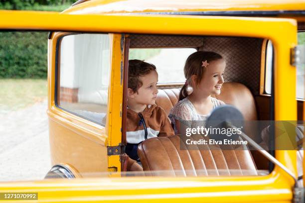 two children sitting in the back seat of a yellow vintage car - carro antigo imagens e fotografias de stock