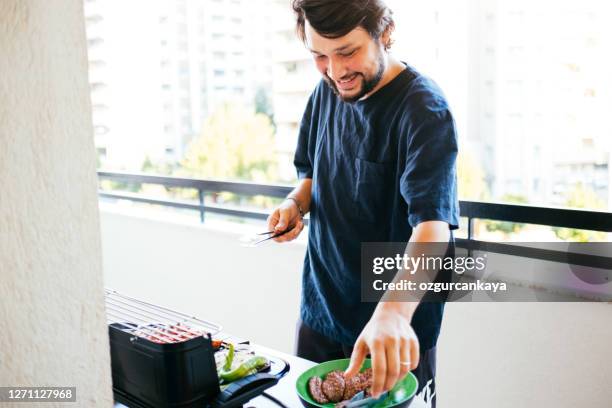 erwachsener mann bereitet essen auf dem grill - grillen balkon stock-fotos und bilder