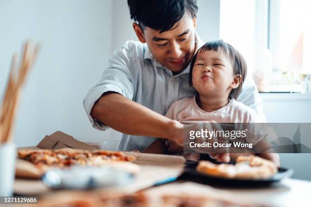 young father feeding food for his baby daughter at the table - chinese family taking photo at home stock-fotos und bilder