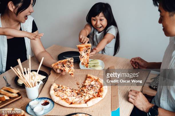 cheerful young girl holding a slice of pizza, sharing meal with family - pizza share bildbanksfoton och bilder
