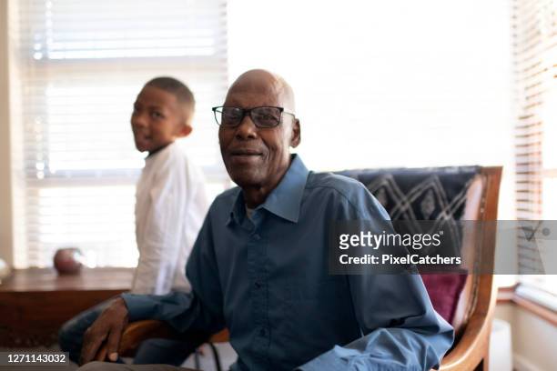 candid portrait grandfather sitting in living room with grandson - black family reunion stock pictures, royalty-free photos & images