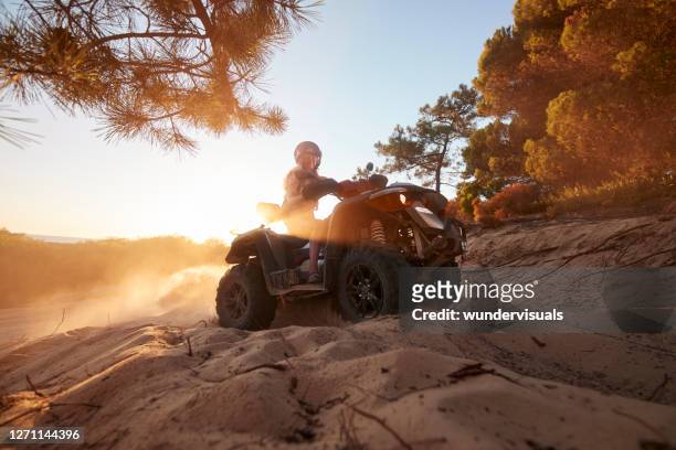 日没時に砂の森の丘の上にクワッドバイクに乗ってヘルメットを身に着けている若い女性 - quadbike ストックフォトと画像