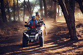 Two friends wearing helmets having fun and riding quad bikes together in the forest
