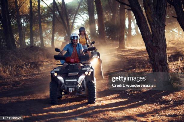 two friends wearing helmets having fun and riding quad bikes together in the forest - off road vehicle imagens e fotografias de stock