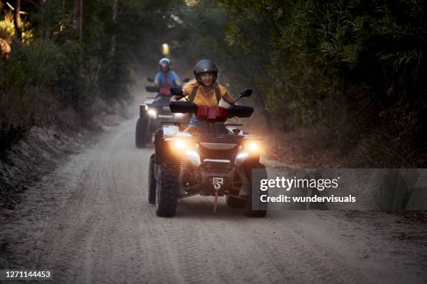 jonge vrouw die het dragen van helm glimlacht die zich terwijl het drijven van quad in het bos bevindt - atv trail stockfoto's en -beelden