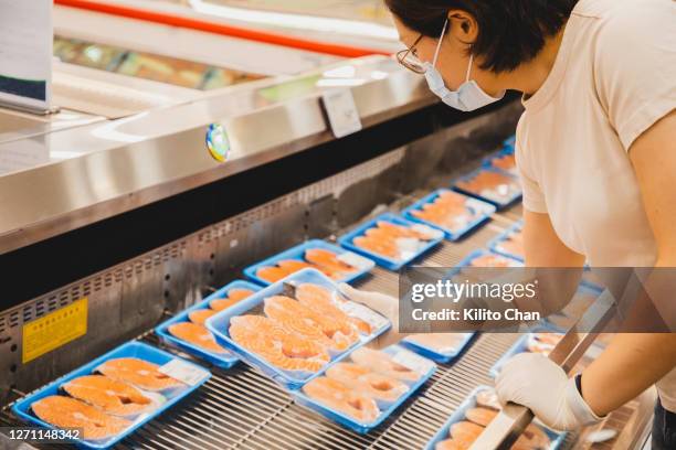 asian female wearing face mask buying fresh salmon - viswinkel stockfoto's en -beelden