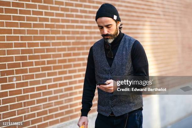 Guest wears a black beanie hat, a gray wool vest, a black turtleneck pullover, outside Fendi, during Milan Fashion Week Menswear Fall/Winter...