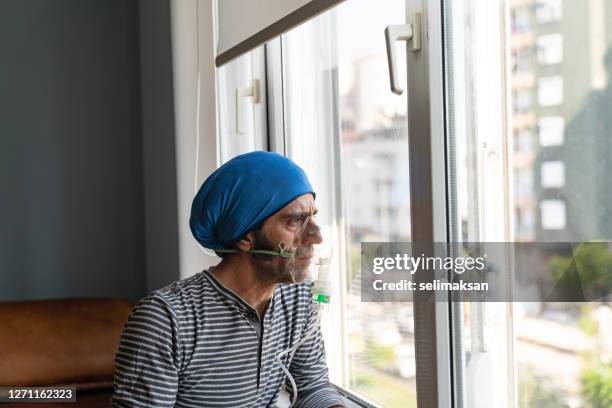 rijpe volwassen mens die verneveler gebruikt en door venster kijkt - copd patient stockfoto's en -beelden