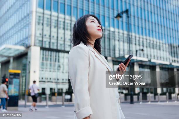 determined businesswoman looking up while using smart phone - japanese bussiness woman looking up imagens e fotografias de stock