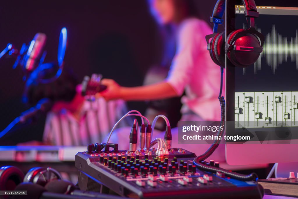 Close up instruments ,musician is background. Headphones hang on microphone with sound mixer board in home recording studio.