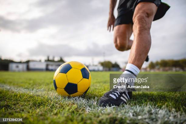 low angle action portrait of footballer running to kick ball - studded imagens e fotografias de stock
