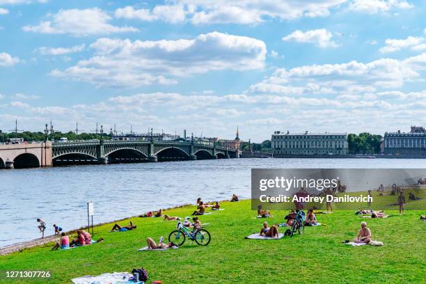 gente relajándose en el césped de la fortaleza de pedro y pablo, san petersburgo. - neva river fotografías e imágenes de stock