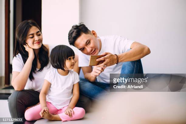 father, mother and daughter looking at a smartphone - kids fun indonesia stock-fotos und bilder
