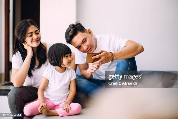 father, mother and daughter looking at a smartphone - malay archipelago stock pictures, royalty-free photos & images