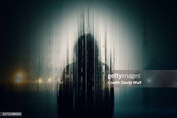 a double exposure of a silhouette of a mysterious hooded figure without a face, in a city at night. with a glitch, edit - crime fotografías e imágenes de stock