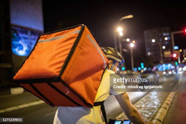delivery person cycling through city streets on his way to customer at night - night delivery stock pictures, royalty-free photos & images