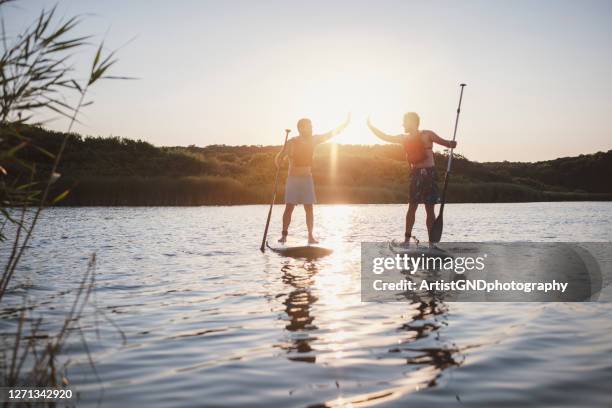 twee jonge mannetjes zijn paddleboarding at the ocean , high five en good emotion - people swim river stockfoto's en -beelden