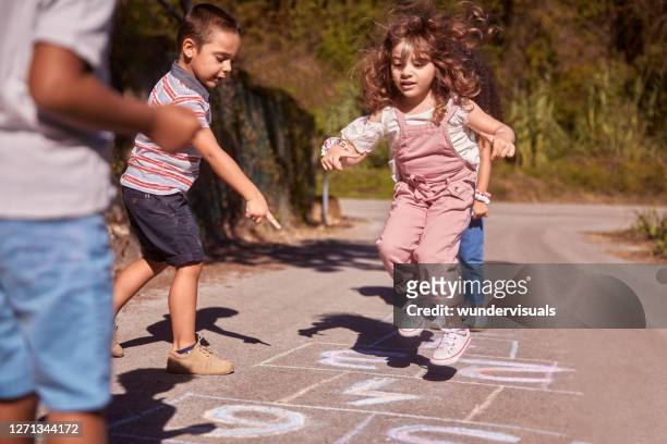 gruppe von kindern mit spaß spielen hopscotch auf der straße - hopscotch stock-fotos und bilder