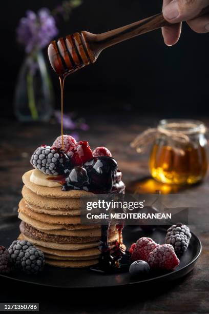 pannekoeken die giet ahornstroop op bevroren bessen gieten - maple syrup pancakes stockfoto's en -beelden