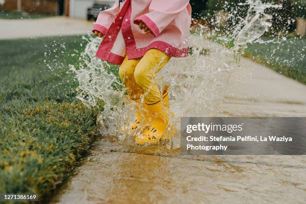 little girl jumping in a big puddle - children jumping stock-fotos und bilder