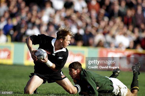 Jeff Wilson of New Zealand looks for support as he is grounded by Pieter Rossouw of South Africa during the Tri-Nations match at Athletic Park in...