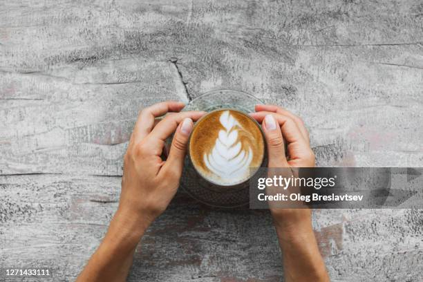 cup of cappuccino in woman hand on gray shabby wooden background - cappuccino top view stock-fotos und bilder