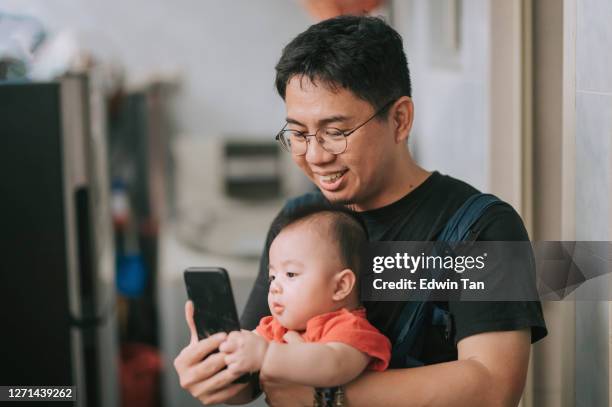 asian chinese parent at home with baby boy doing selfie looking at camera with baby carrier - baby text stock pictures, royalty-free photos & images