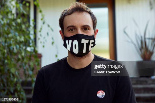 portrait of a man sitting in front of his house, wearing a vote facemask, looking into camera smiling. - voting mask stock pictures, royalty-free photos & images