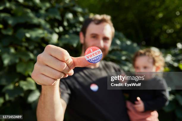 a father standing outside holding his baby, with an "i voted sticker" on his thumb - genderblend stock-fotos und bilder