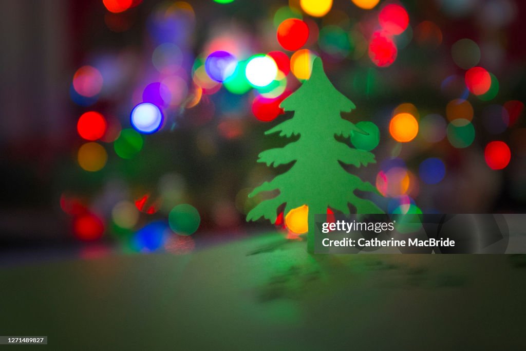 Paper Christmas Tree Cut-Out In Front Of Christmas Tree Lights