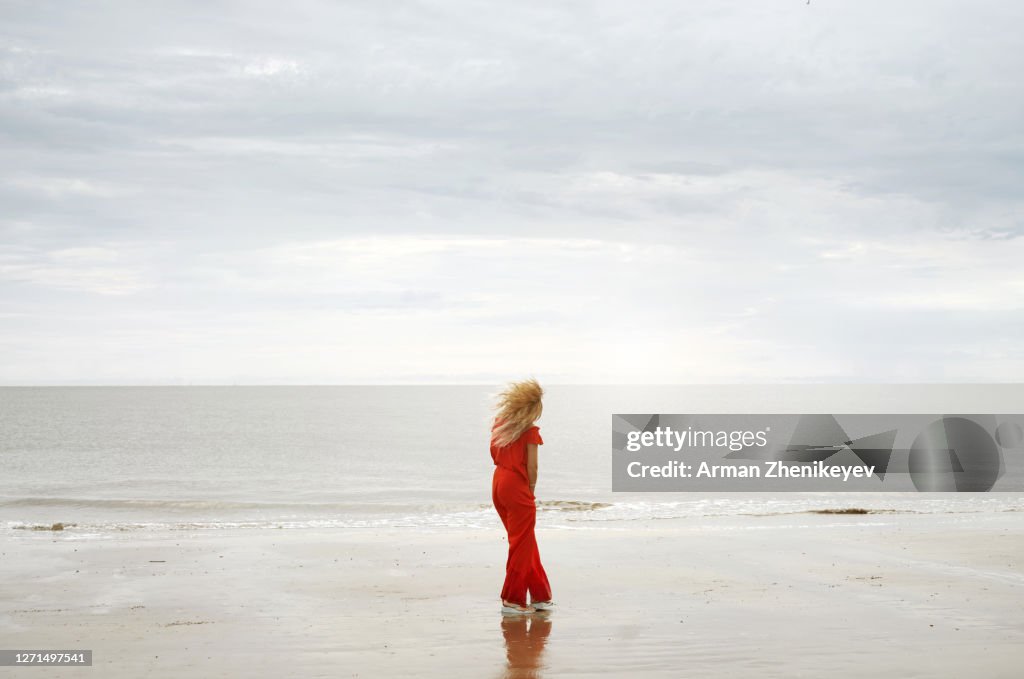 Back view on a serene woman next to the ocean wearing red trouser suit