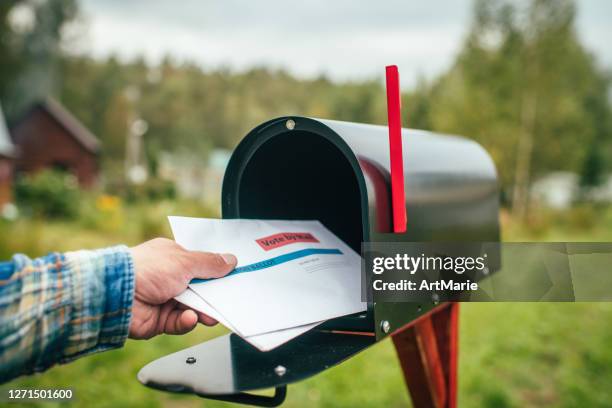 nahaufnahme der hand des mannes senden oder empfangen brief mit stimmzettel in der nähe eines briefkastens in der nähe seines hauses - briefkasten stock-fotos und bilder