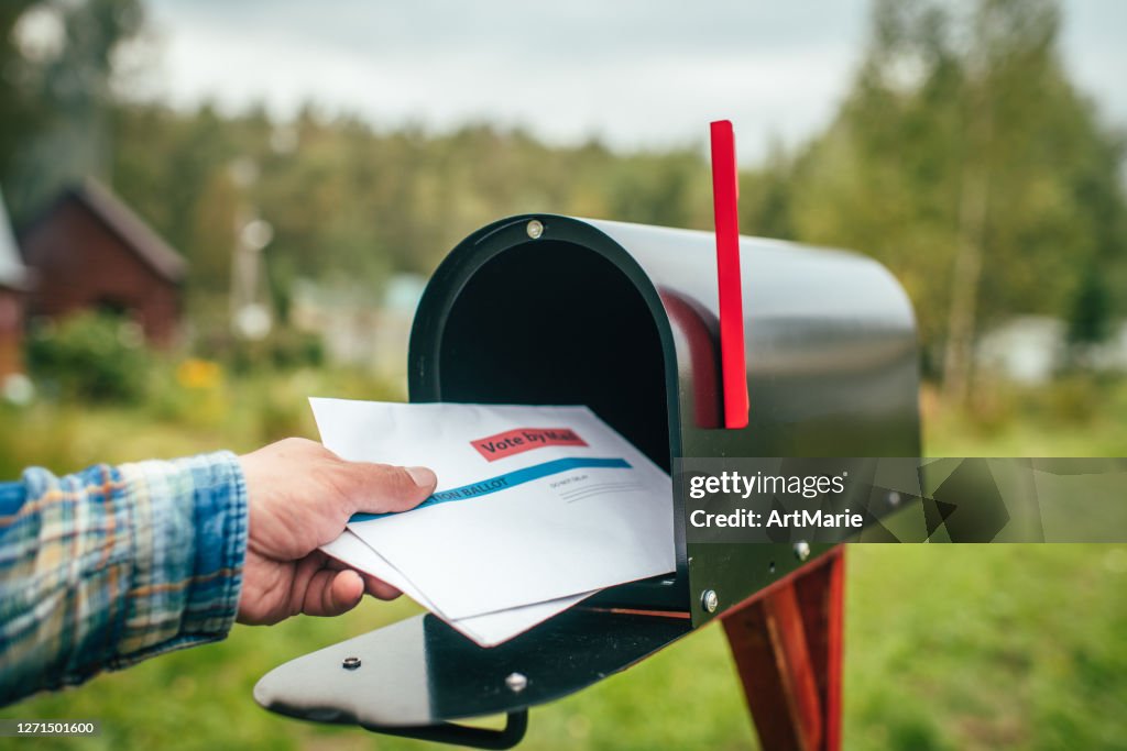 Close-up of man's hand sending or receiving letter with voting ballot near a mailbox near his house