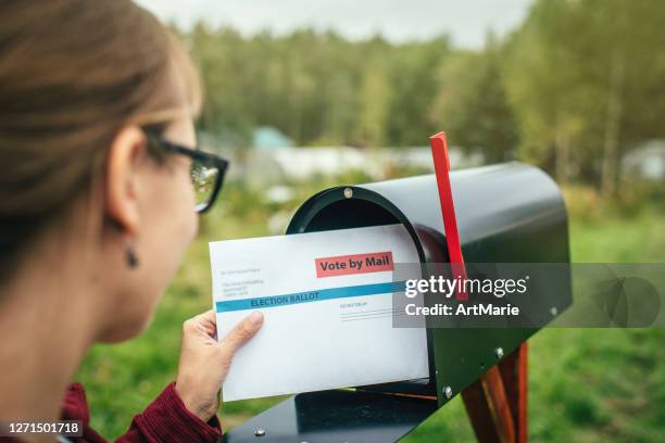 woman sending or receiving letter with voting ballot near a mailbox near her house - mail ballot stock pictures, royalty-free photos & images